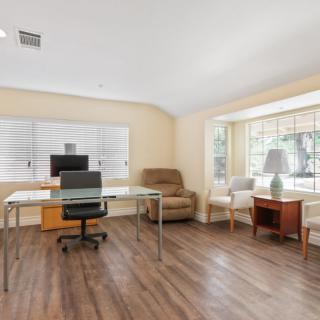 A spacious office workspace with a modern desk, chair, and computer monitor, featuring large windows and wood flooring.