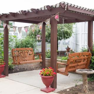 A charming backyard pergola with two wooden swings surrounded by lush greenery and decorative flower pots.