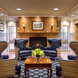 A cozy lounge area featuring blue armchairs, a central fireplace, and a wooden coffee table with fresh flowers.