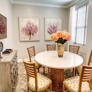 A cozy dining room featuring a round table with wooden chairs, adorned by a vase of flowers, and complemented by wall art.