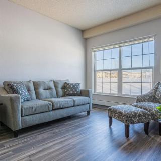 A cozy living room with a sofa, chair, and ottoman by a large window.
