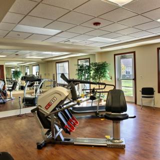 A well-lit gym with various exercise equipment and a wooden floor.