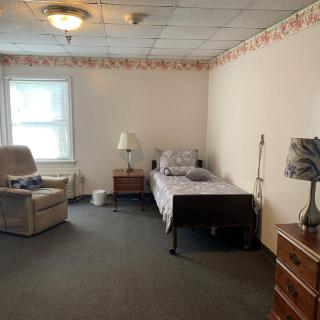 A simple bedroom with a single bed, armchair, and nightstands under soft lighting.