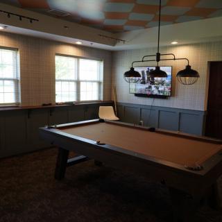 A cozy game room featuring a pool table and overhead lights, with a television on the wall.