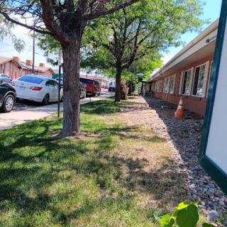 A view of a landscaped area alongside a row of buildings, featuring trees and parked cars.