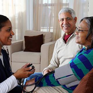 A nurse conducts a health checkup for an elderly couple at home.