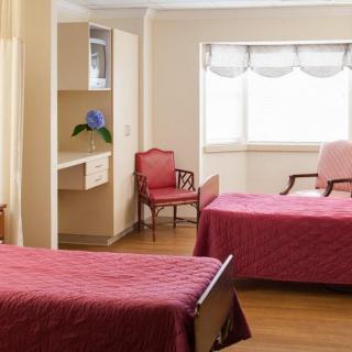 A well-lit shared bedroom with two red-covered beds and classic furniture.