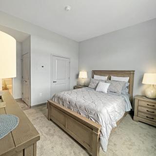 A modern bedroom with neutral tones, featuring a bed with patterned bedding, nightstands, and lamps.