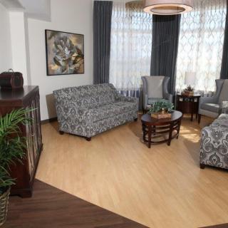 A cozy living room with patterned sofas, armchairs, and a coffee table, complemented by decorative plants and elegant curtains.