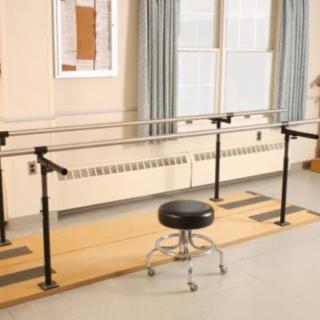A physical therapy room featuring parallel bars and a stool for rehabilitation exercises.
