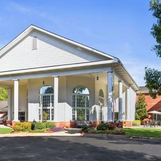 A large white building with columns and a driveway surrounded by trees.