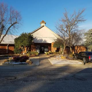 A serene view of a building surrounded by trees and a parking lot under clear blue skies.