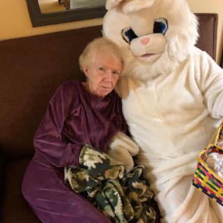 An elderly woman enjoys a moment with an Easter Bunny mascot, sharing smiles and warmth.