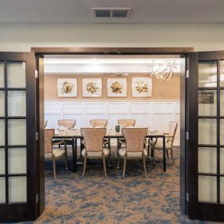A well-lit dining room with a large table surrounded by chairs, decorated with framed artwork on the walls.