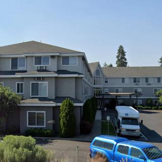 A residential building with a parking lot and several vehicles parked in front, set against a clear blue sky.