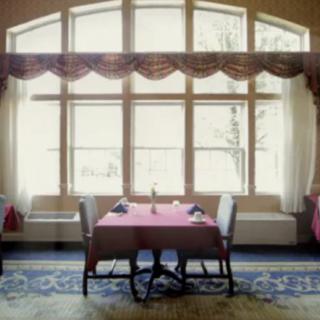 A cozy restaurant interior with a table and chairs by a large window.