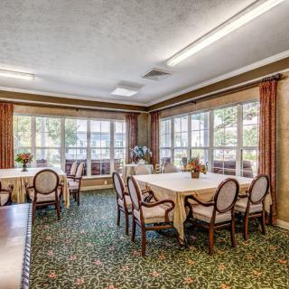 A well-lit dining room with tables and chairs surrounded by large windows and decorated with curtains.