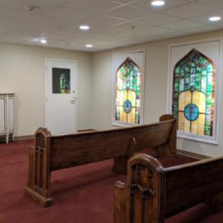 A small chapel interior featuring wooden pews and colorful stained glass windows.