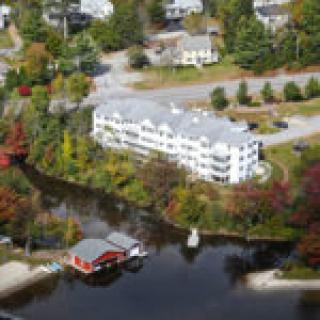 An aerial view of a waterfront building surrounded by trees with vibrant autumn foliage.