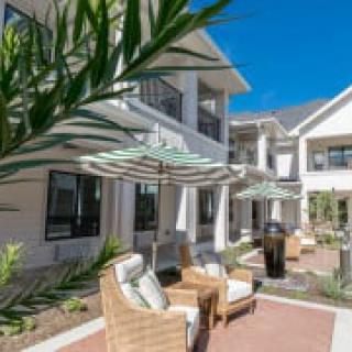 A modern patio with comfortable seating and umbrellas outside a contemporary house.