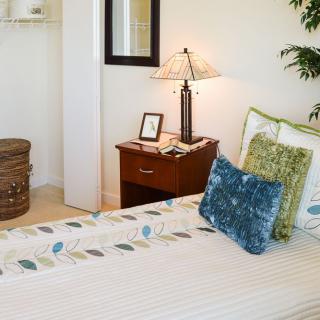A cozy bedroom interior featuring a neatly made bed with decorative pillows and a nightstand adorned with a lamp.