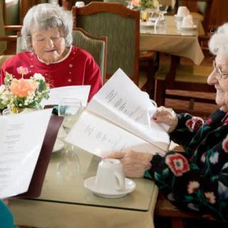 Two elderly women sitting at a restaurant table, looking at menus.