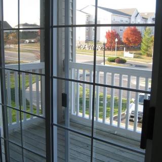 A view from inside looking out through glass doors onto a balcony, with a suburban street and autumn trees visible in the distance.
