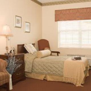 A cozy bedroom with a single bed, bedside table, lamp, armchair, and window.