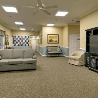 A comfortable lounge area featuring sofas, armchairs, a television, and a ceiling fan.