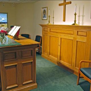 A small chapel with an altar, candles, and a cross on the wall, arranged for prayer.