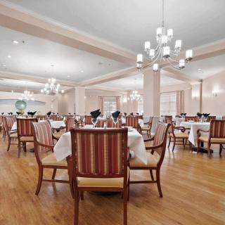 An elegant dining room with neatly arranged tables and chairs, illuminated by chandeliers.