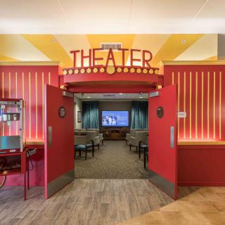 A vibrant theater entrance with red decor leading to a cozy seating area and a screen.