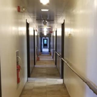 A long indoor hallway with multiple doors on each side and overhead lighting.
