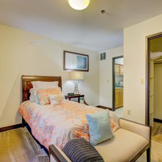 A cozy bedroom featuring a single bed with decorative pillows and a nightstand with a lamp, complemented by a piece of artwork on the wall.
