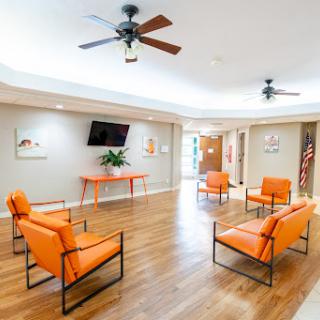 A stylish and inviting waiting area featuring modern orange chairs and wooden flooring, enhanced by ceiling fans for comfort.