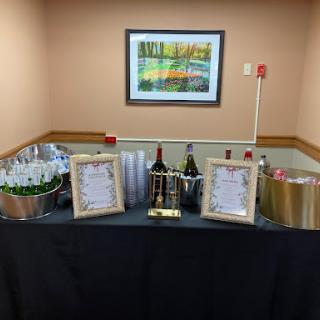 A beautifully arranged beverage station for a celebration, featuring wine bottles, glasses, and framed menus.