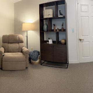A cozy living room corner featuring an armchair, a lamp, and a shelf filled with decorative items.