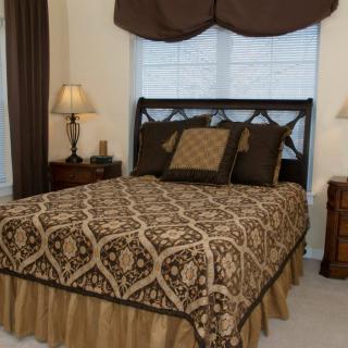 A traditionally decorated bedroom with a patterned bedspread, pillows, and matching drapes.