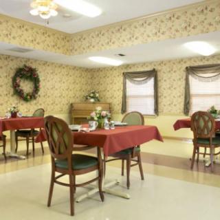 A dining room with floral wallpaper and tables set with red tablecloths.