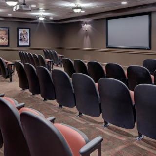 An empty theater room with rows of seats facing a large screen.