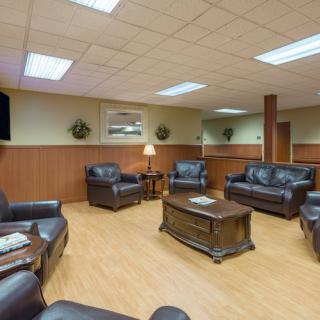 A comfortable waiting room with leather couches and a coffee table, decorated with wood paneling and artwork.