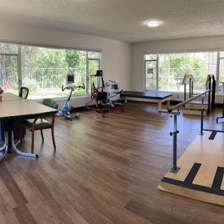 A spacious and well-lit rehabilitation and therapy room equipped with various exercise machines and tables.