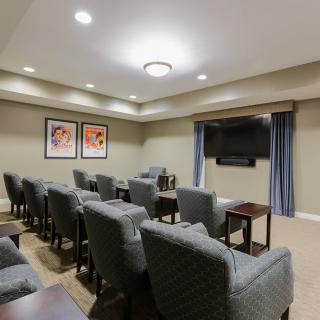 A cozy home theater setup with rows of comfortable chairs facing a large television, adorned with simple decor and soft lighting.