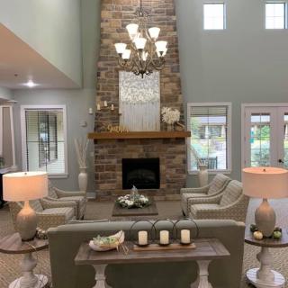 A modern living room featuring a tall stone fireplace and elegant chandelier, surrounded by comfortable seating.