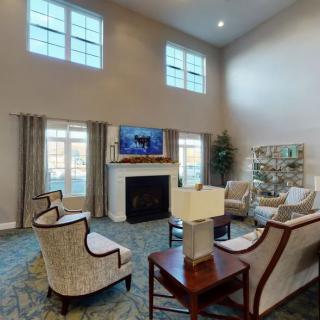 A spacious living room with high ceilings, featuring a large fireplace and arranged seating around a central table.