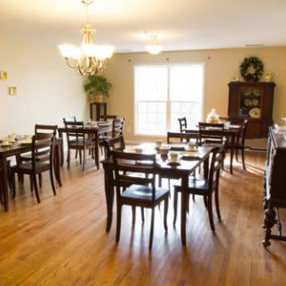 A cozy dining room with arranged tables and chairs, illuminated by natural light from a large window.