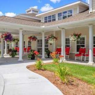 A charming building with a porch adorned with red chairs and hanging flower baskets.