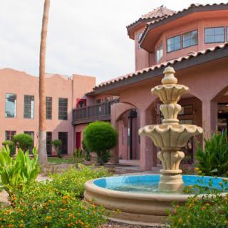 A beautiful courtyard with a central fountain surrounded by greenery and a large building.