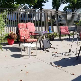 A sunny backyard patio with chairs and a table near a fence.