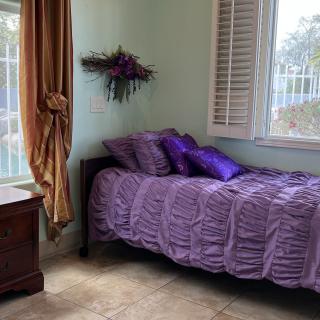 Cozy bedroom with a purple-themed single bed and natural lighting.